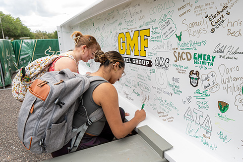 Two students sign beam for new on-campus stadium.