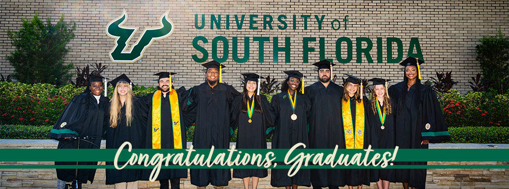 a group of 10 graduates in their regalia in front of the USF logo on the side of SVC building with "Congratulations, Graduates!"