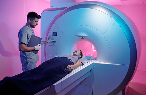 woman lying on MRI cot while tech stands beside the machine