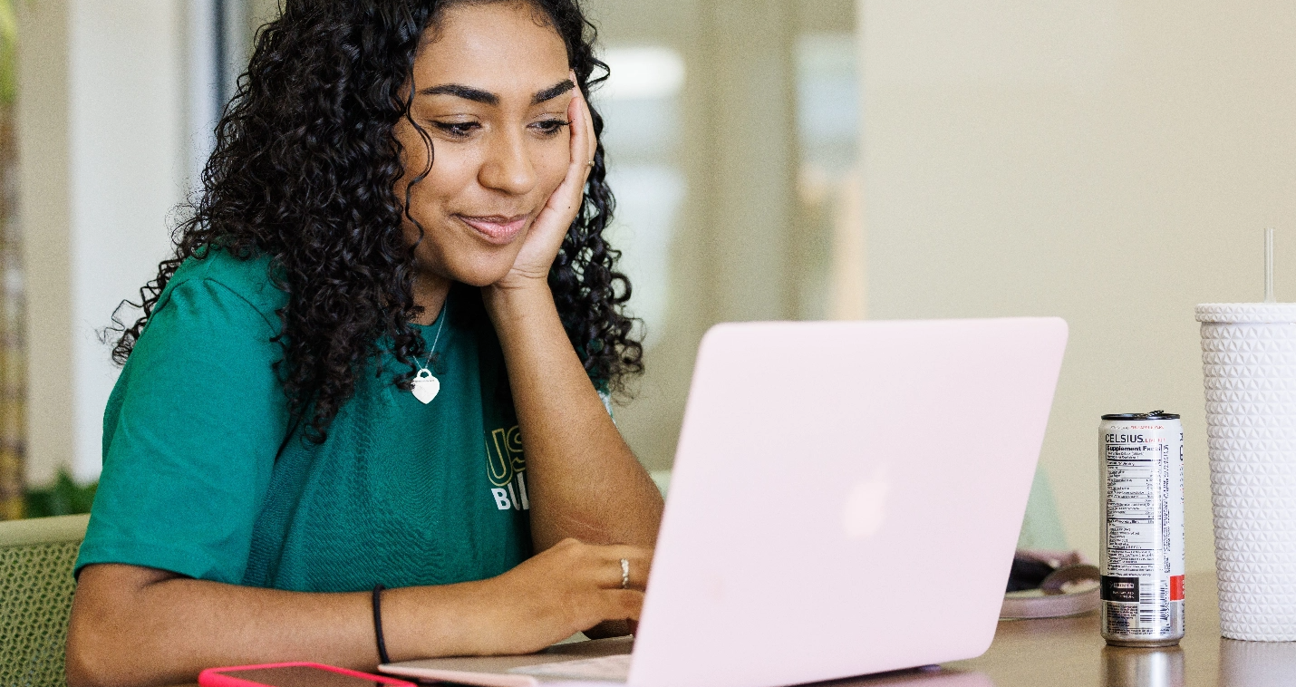USF student in a green shirt sitting at a table and using her laptop.